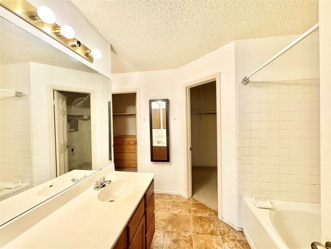 Full bath featuring vanity, a walk in closet, a textured ceiling, and washtub / shower combination | Image 16