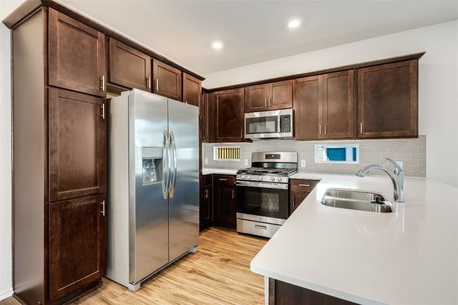 Kitchen with appliances with stainless steel finishes, light countertops, light wood-style flooring, dark brown cabinets, and decorative backsplash | Image 12