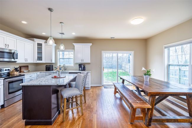 Kitchen featuring stainless steel appliances, a center island, a kitchen bar, glass insert cabinets, and white cabinetry | Image 9