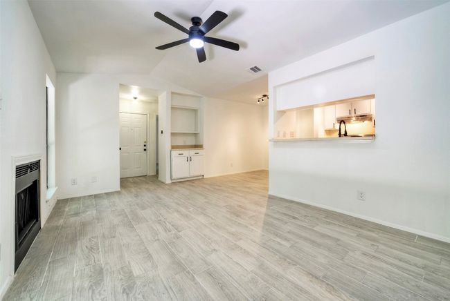 Unfurnished living room with a ceiling fan, light wood finished floors, a fireplace, heating unit, and lofted ceiling | Image 5