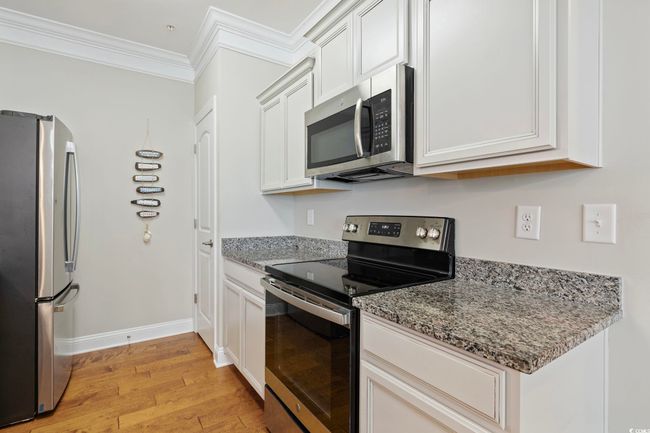 Kitchen featuring appliances with stainless steel finishes, light wood-style flooring, ornamental molding, stone counters, and white cabinets | Image 10