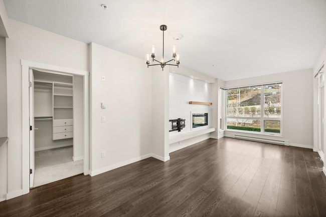 Unfurnished living room with a chandelier, baseboard heating, dark wood finished floors, and a large fireplace | Image 6