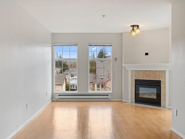 Unfurnished living room featuring baseboards, wood finished floors, a baseboard heating unit, and a tile fireplace | Image 7
