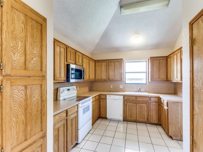Kitchen with white appliances, a textured ceiling, lofted ceiling, light countertops, and light tile patterned floors | Image 21