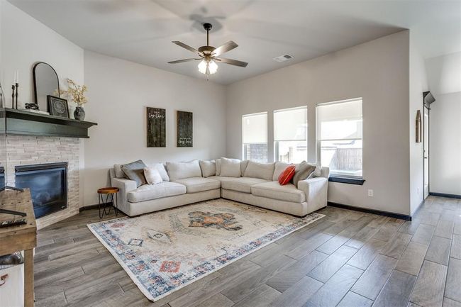 Living room with a ceiling fan, a glass covered fireplace, wood finished floors, and visible vents | Image 42