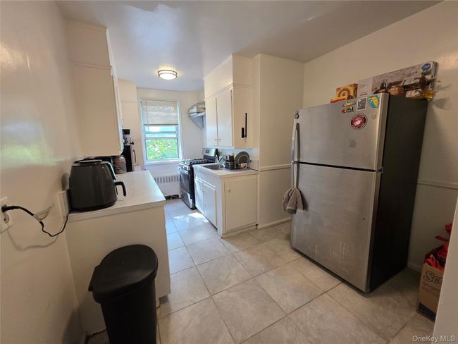 Kitchen with stainless steel appliances, radiator, light countertops, white cabinetry, and light tile patterned flooring | Image 4
