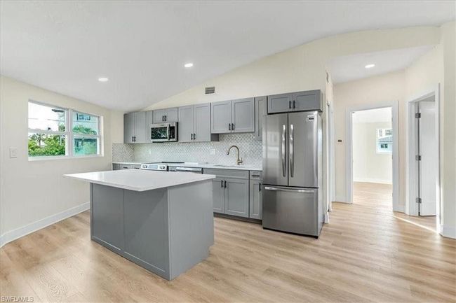 Kitchen featuring stainless steel appliances, gray cabinets, light countertops, a kitchen island, and decorative backsplash - Virtually edited | Image 12