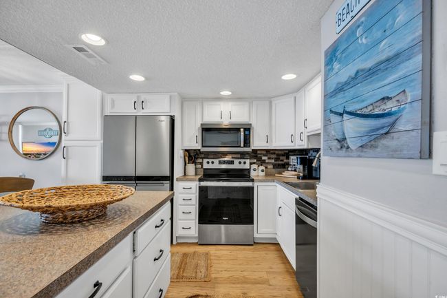 Kitchen featuring stainless steel appliances, crown molding, white cabinets, a textured ceiling, and decorative backsplash | Image 16