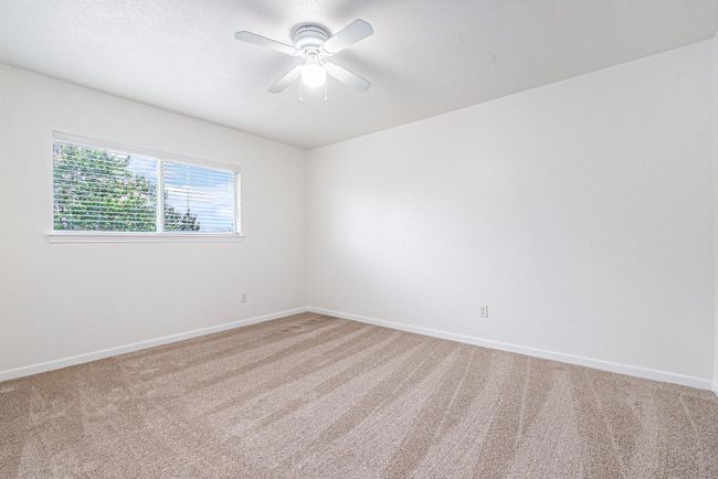 This is a bright bedroom featuring neutral carpeting, a ceiling fan, and a large window with blinds offering natural light. | Image 14