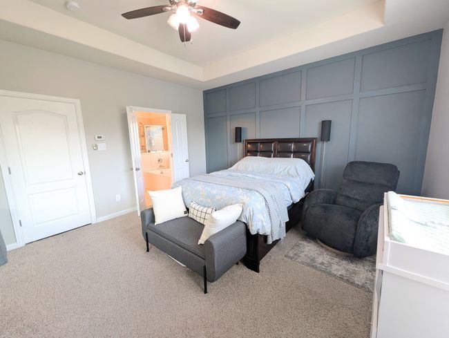 Bedroom featuring a raised ceiling, light colored carpet, ceiling fan, and ensuite bathroom | Image 33