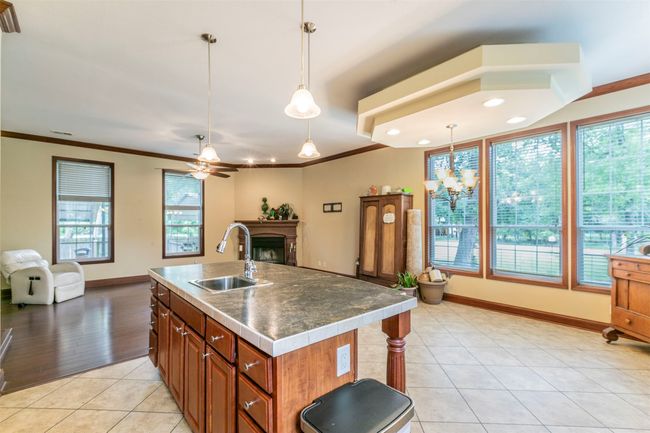 Kitchen featuring open floor plan, a sink, ceiling fan with notable chandelier, and a fireplace | Image 7