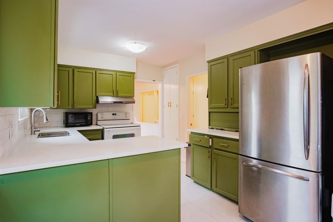 Kitchen with white electric range, under cabinet range hood, a sink, freestanding refrigerator, and green cabinets | Image 12