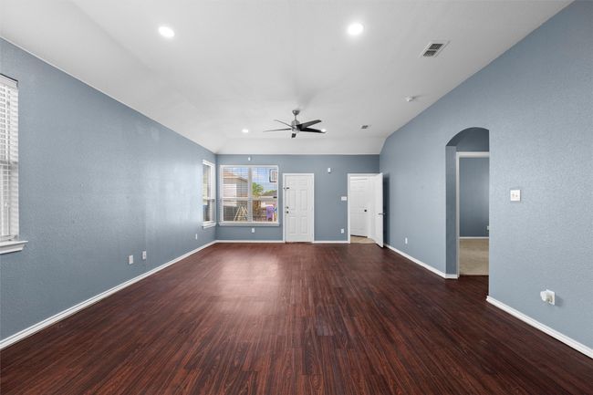 Unfurnished living room with baseboards, a ceiling fan, visible vents, arched walkways, and wood finished floors | Image 17