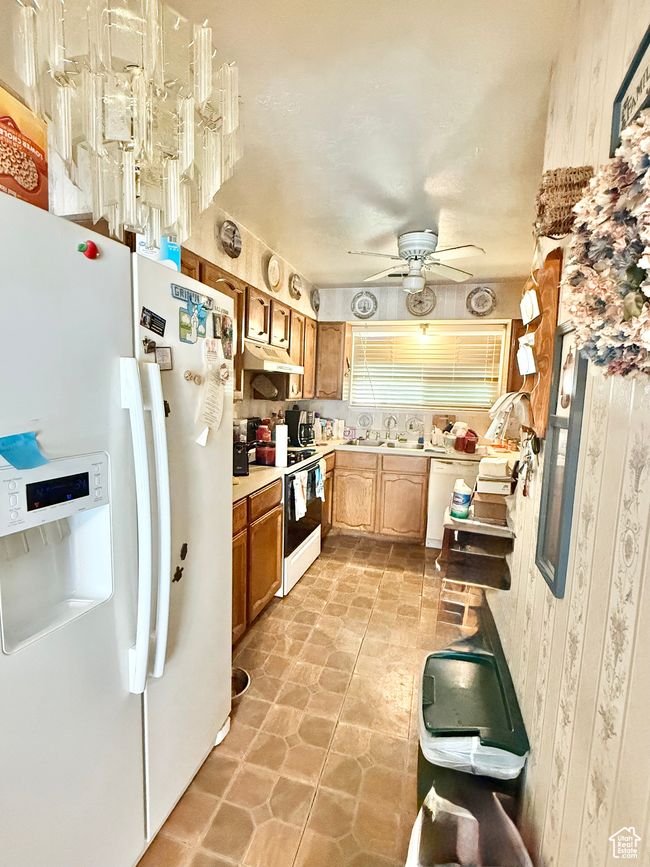 Kitchen with white appliances, under cabinet range hood, light countertops, ceiling fan, and brown cabinetry | Image 4