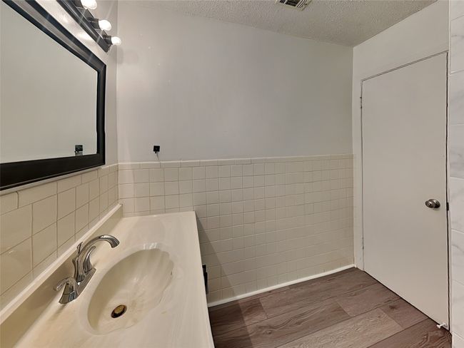 Bathroom with tile walls, wood finished floors, a textured ceiling, vanity, and wainscoting | Image 17