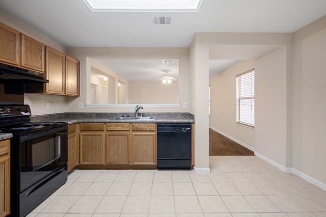 Kitchen with black appliances, under cabinet range hood, ceiling fan, dark countertops, and light tile patterned floors | Image 6