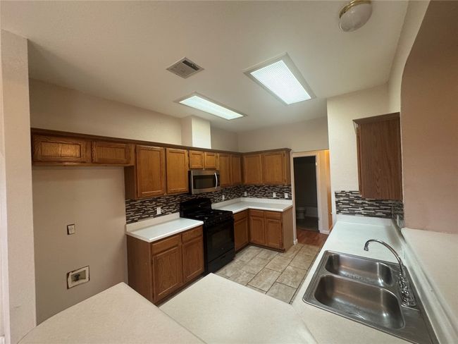 Kitchen featuring black range with gas cooktop, brown cabinets, stainless steel microwave, backsplash, and light countertops | Image 5