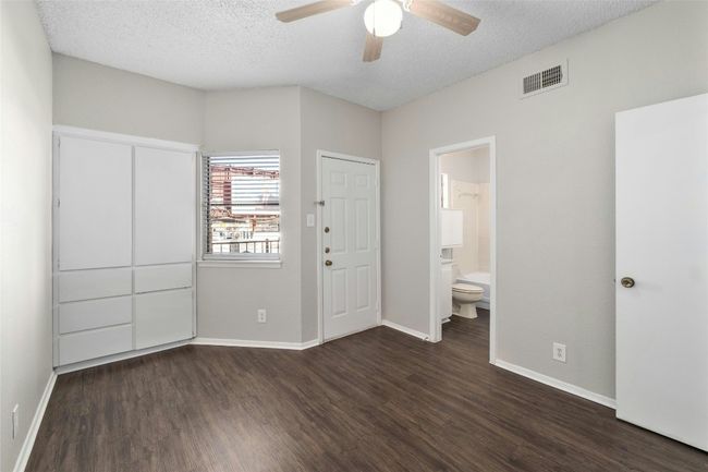 Unfurnished bedroom with baseboards, ensuite bathroom, dark wood-style floors, visible vents, and a textured ceiling | Image 17