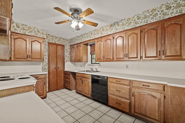 Kitchen featuring wallpapered walls, a sink, dishwasher, a ceiling fan, and brown cabinetry | Image 13