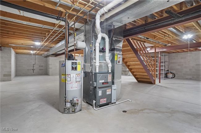 Unfinished basement with concrete block wall, heating unit, water heater, and stairs | Image 43