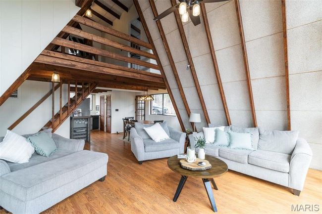 Living room with beam ceiling, high vaulted ceiling, wood finished floors, stairway, and ceiling fan | Image 7
