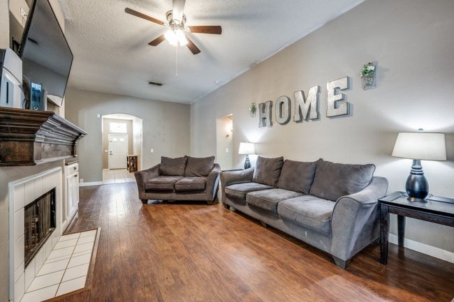 Living room featuring ceiling fan, wood finished floors, arched walkways, a fireplace, and a textured ceiling | Image 4