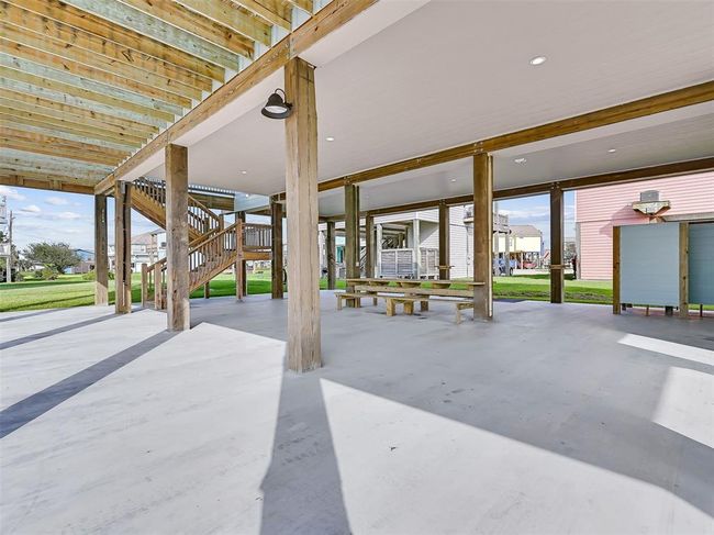 The ground-level features a single-bay garage for storage plus a spacious covered area with an enclosed outdoor shower and a built-in picnic table with benches—ideal for outdoor games, dining, or shaded relaxation after a day at the beach. | Image 28