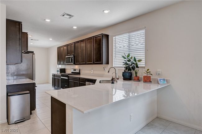 Kitchen featuring appliances with stainless steel finishes, a sink, dark brown cabinets, light countertops, and a peninsula | Image 11