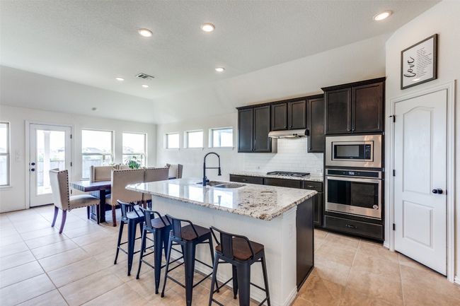 Kitchen featuring appliances with stainless steel finishes, a kitchen breakfast bar, decorative backsplash, light stone counters, and a center island with upgraded sink fixture | Image 8