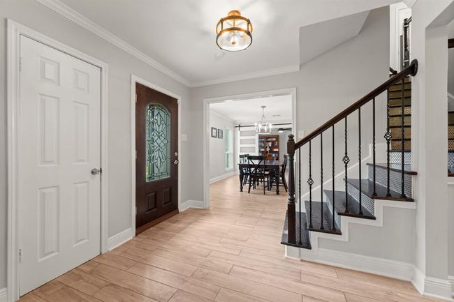 This welcoming entryway showcases a stylish wooden door with decorative glass and a staircase accented by an elegant railing leading to the upper level. | Image 5