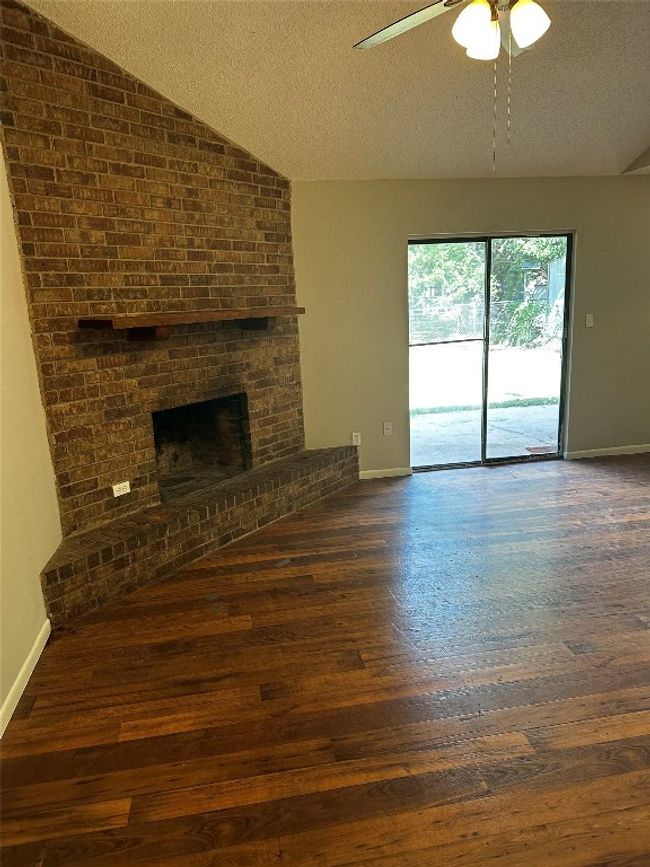 Unfurnished living room with lofted ceiling, a textured ceiling, a brick fireplace, hardwood / wood-style floors, and ceiling fan | Image 7