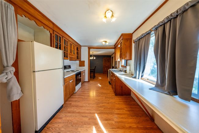 Kitchen featuring freestanding refrigerator, electric stove, brown cabinets, a chandelier, and glass insert cabinets | Image 10
