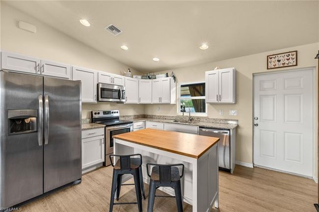 Kitchen featuring vaulted ceiling, a kitchen breakfast bar, appliances with stainless steel finishes, visible vents, and wood counters | Image 6