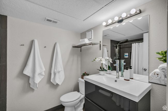 Full bathroom with toilet, vanity, a shower with shower curtain, and a textured wall | Image 19