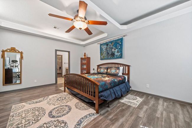 Bedroom with a tray ceiling, visible vents, baseboards, and wood finished floors | Image 16
