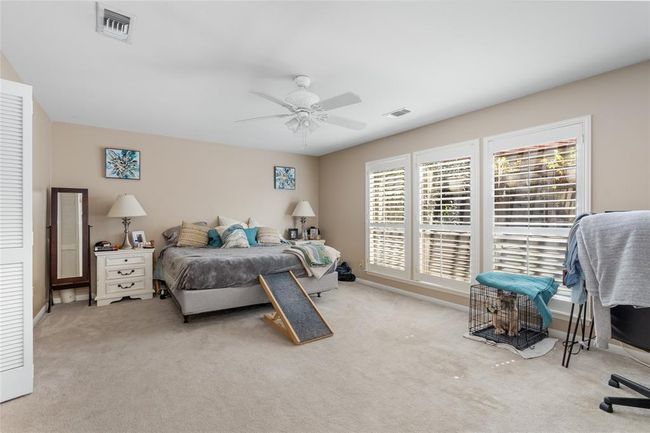 This spacious primary bedroom offers a serene retreat with soft neutral tones, plush carpeting, and abundant natural light streaming through large windows adorned with plantation shutters. The generous layout provides ample space for relaxation, while the ceiling fan ensures year-round comfort. | Image 23