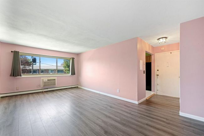 Unfurnished living room with baseboards, a baseboard heating unit, wood finished floors, and a wall mounted air conditioner | Image 10