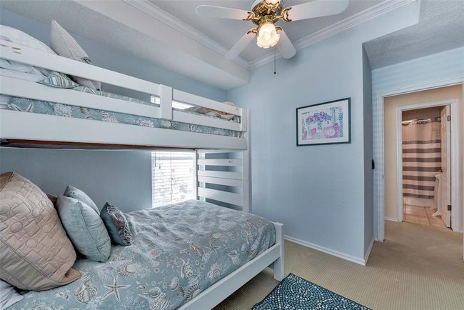 Upstairs bedroom features soft coastal tones, crown molding, and easy access to a full bath. A relaxing space for guests or family | Image 18