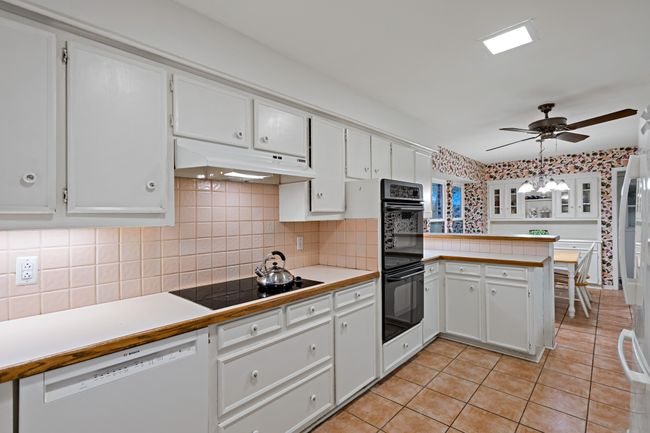 Kitchen featuring a peninsula, white cabinetry, light tile floors, under cabinet range hood, and appliances | Image 13