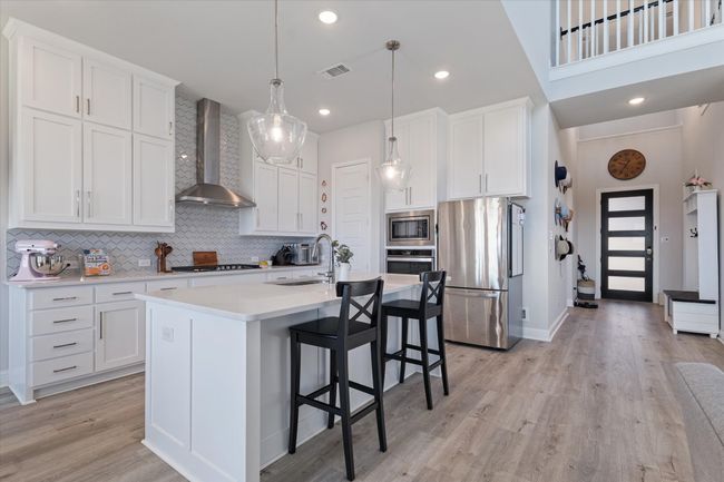 Kitchen featuring appliances with stainless steel finishes, wall chimney exhaust hood, a sink, decorative backsplash, and white cabinetry | Image 9