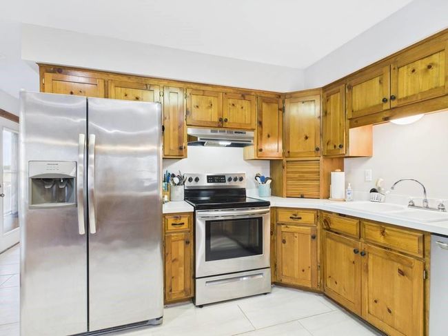 Kitchen featuring light countertops, under cabinet range hood, wood cabinets, stainless steel appliances, and a sink | Image 39