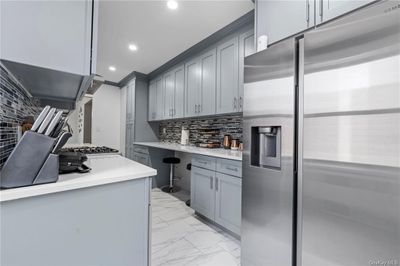 Kitchen featuring gray cabinets, crown molding, stainless steel refrigerator with ice dispenser, and tasteful backsplash | Image 3