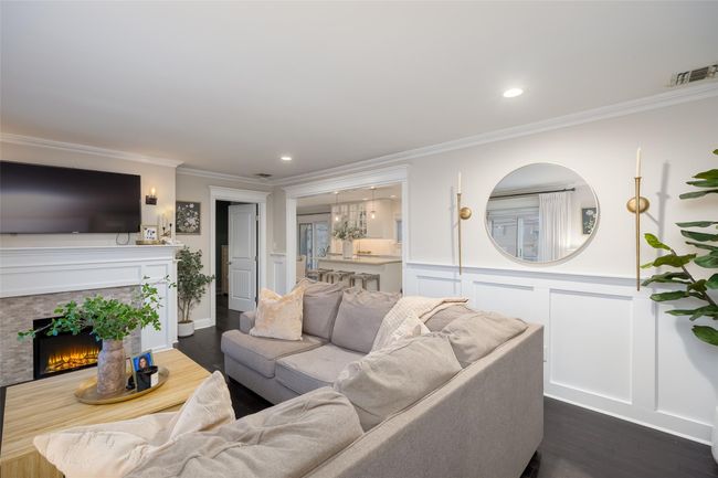Living area with dark wood-type flooring, a decorative wall, visible vents, and ornamental molding | Image 11