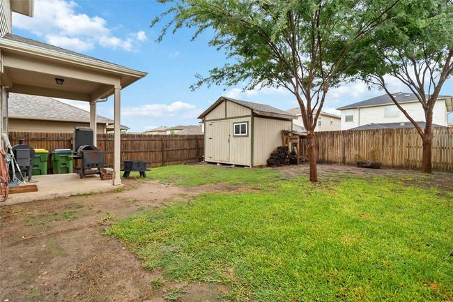 Fenced backyard with a storage shed and a covered patio. | Image 14