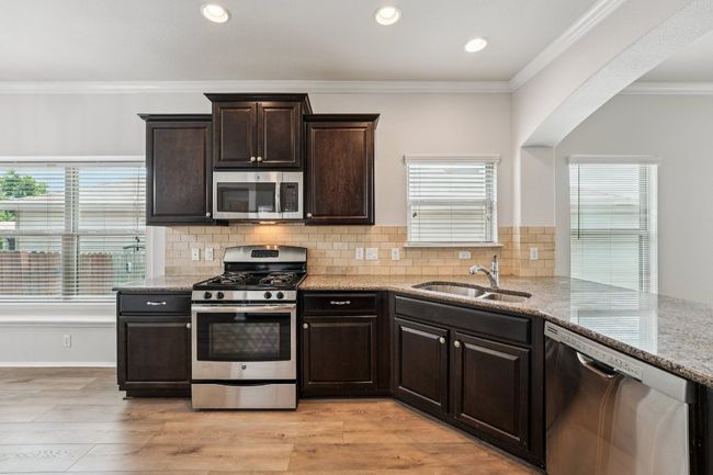 Kitchen featuring appliances with stainless steel finishes, a sink, light stone countertops, dark brown cabinets, and tasteful backsplash | Image 13