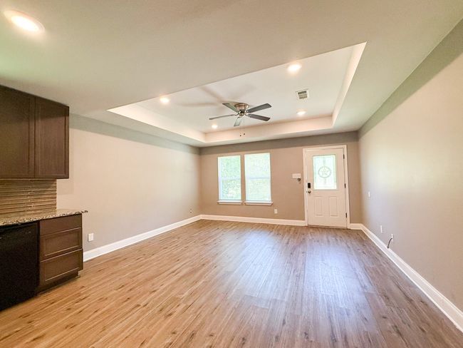 Unfurnished living room with a tray ceiling, light wood-type flooring, ceiling fan, and recessed lighting | Image 6