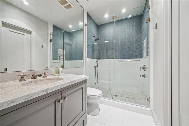 Stylish secondary ensuite bath features a wide vanity topped with marble, polished hardware, and a glass-enclosed walk-in shower. The shower is finished with striking Thorntree tile, offering a modern, textural contrast that elevates the space. Thoughtful design and high-end finishes create a spa-like atmosphere to be enjoyed daily. | Image 31