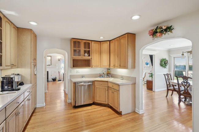 Kitchen featuring glass insert cabinets, arched walkways, light countertops, light wood-type flooring, and stainless steel dishwasher | Image 13