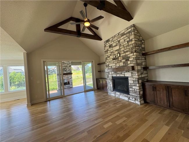 Unfurnished living room with a stone fireplace, plenty of natural light, light wood-style floors, high vaulted ceiling, and beam ceiling | Image 24