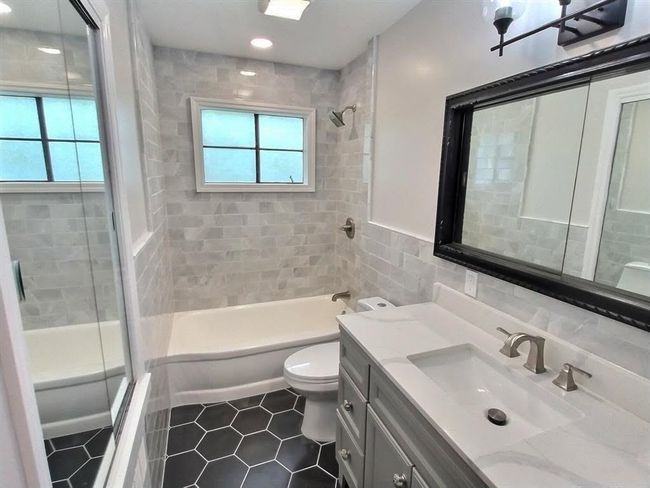 Full bath featuring toilet, shower / tub combination, vanity, tile patterned floors, and tile walls | Image 21